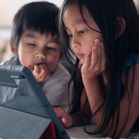 A young boy and girl are looking at a tablet screen.